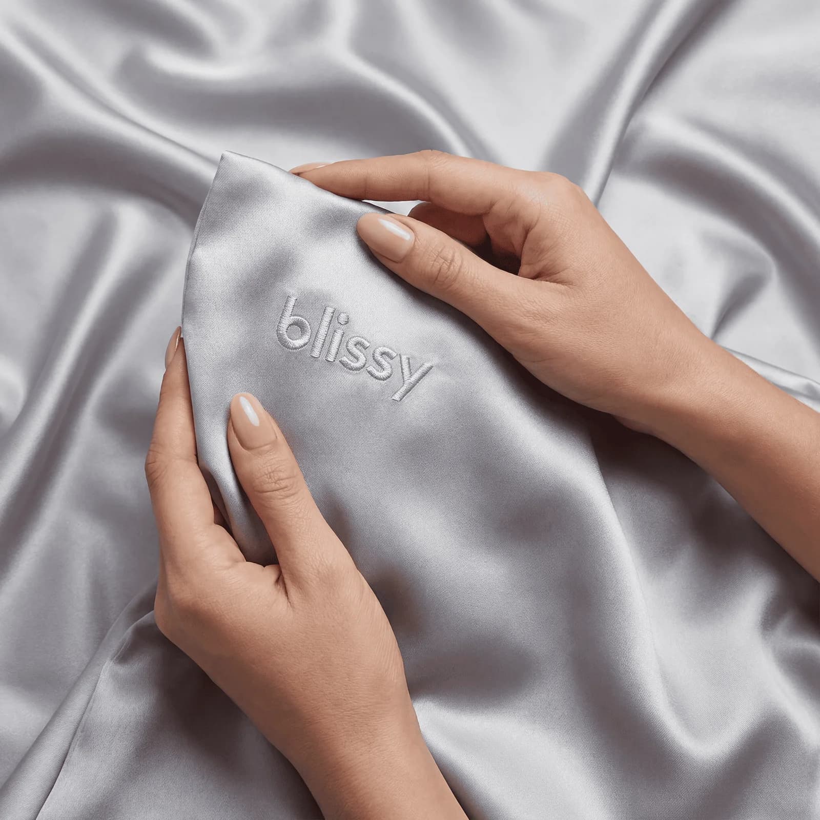Hands showing the embroidered edge of a Blissy Silver silk pillowcase