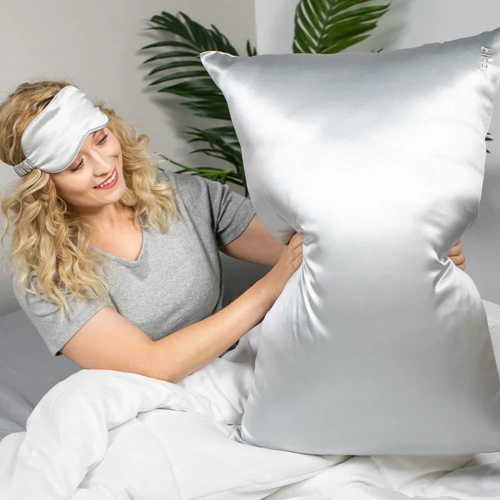 Woman holding a Blissy Silver silk pillowcase in a bedroom